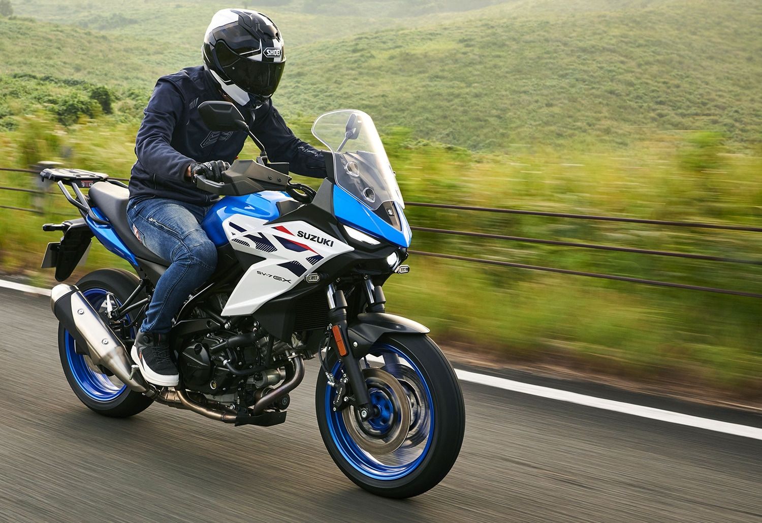 Fahrer mit Helm auf der blau-weißen Suzuki SV-7GX vor Waldhintergrund