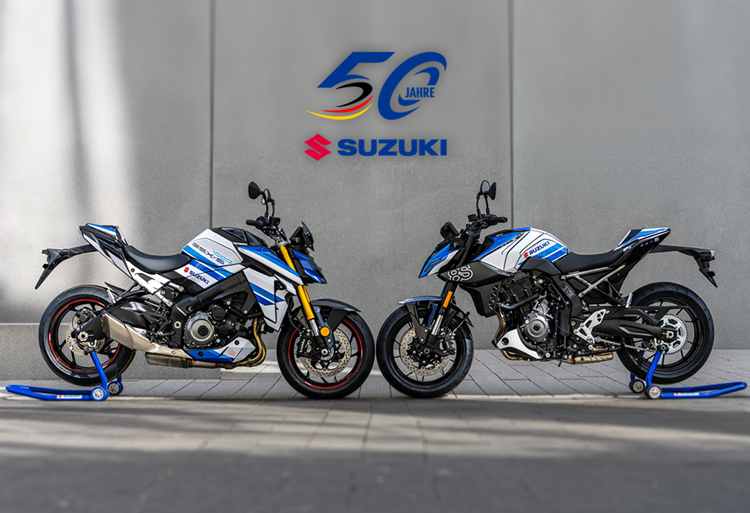 Die Suzuki GSX-S1000 und GSX-8S Special Edition nebeneinander auf Montageständern vor einer Wand mit dem „50 Jahre Suzuki“-Jubiläumslogo.
